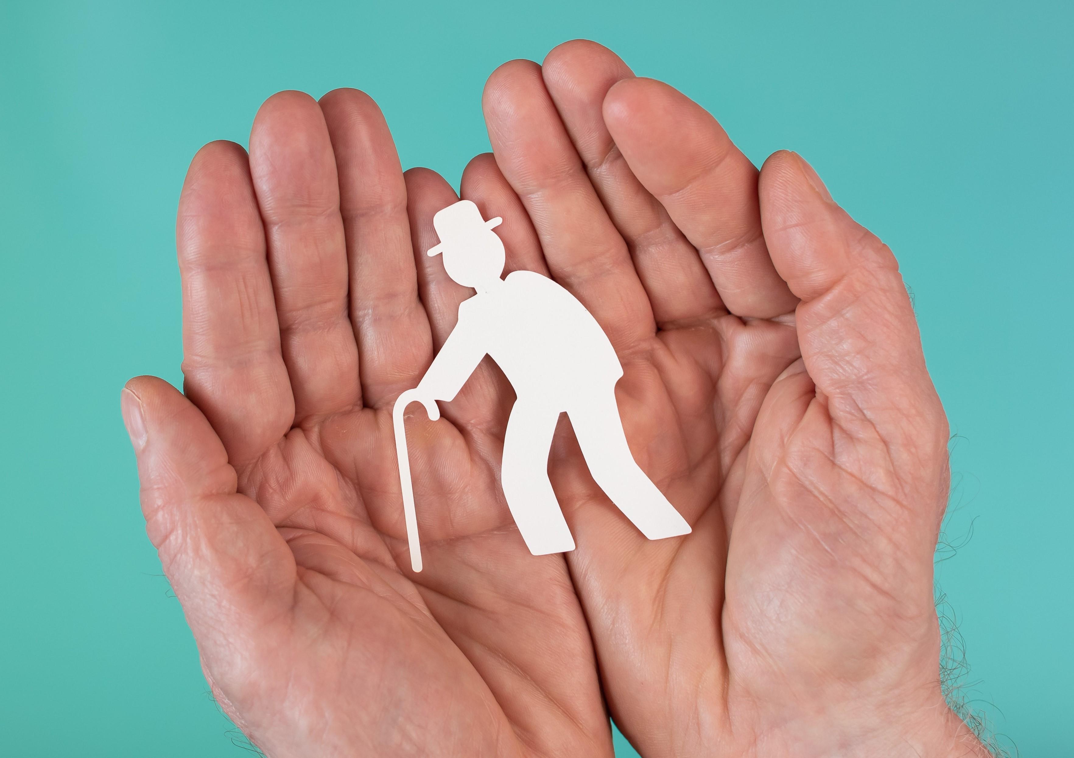 Main protégeant une silhouette en papier d'un sénior